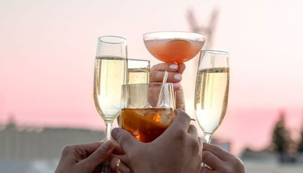 hands holding various cocktails toasting during sunset